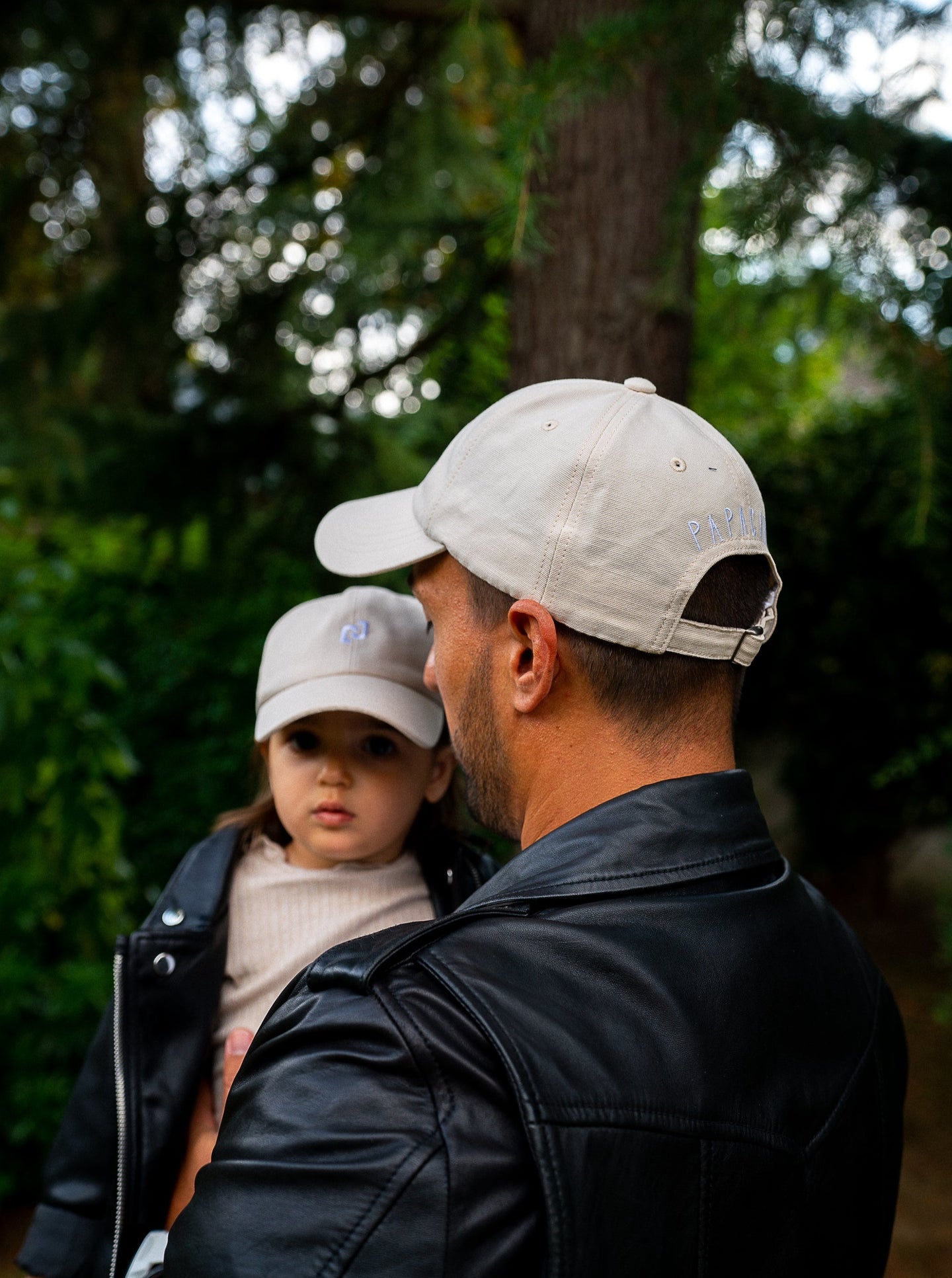 Un papa et sa fille profitant d'un moment complice, tous deux portant des casquettes assorties et stylées.